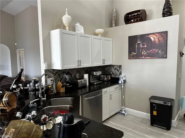 Kitchen featuring dark stone counters, stainless steel dishwasher, tasteful backsplash, white cabinets, and a textured wall