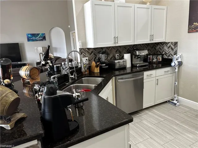 Kitchen featuring dark stone counters, open floor plan, dishwasher, white cabinetry, and a textured wall