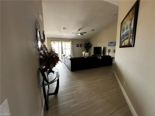 Living room with vaulted ceiling, wood finished floors, a textured wall, and a ceiling fan