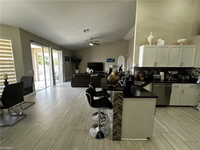 Kitchen with a peninsula, a kitchen breakfast bar, open floor plan, white cabinetry, and stainless steel dishwasher