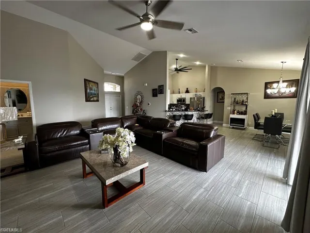 Living room featuring arched walkways, high vaulted ceiling, a chandelier, and ceiling fan
