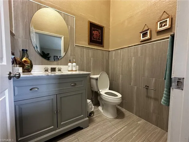Half bath with a textured wall, vanity, and tile walls
