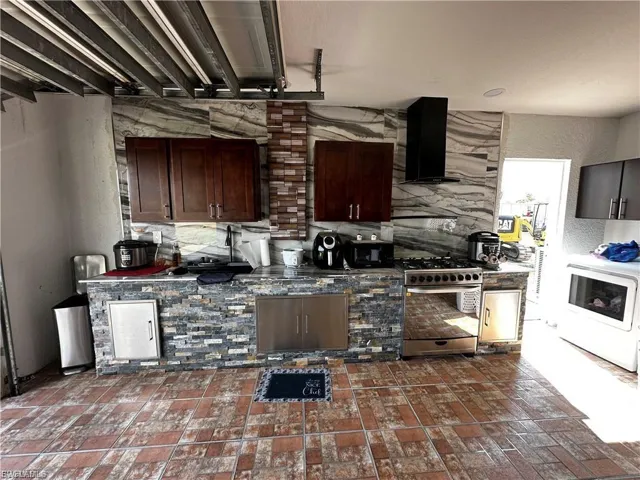 Kitchen with a textured wall, gas stove, wall chimney range hood, washer / clothes dryer, and dark brown cabinets