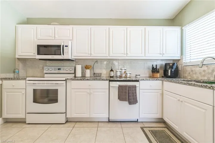 Kitchen with white cabinetry, tasteful backsplash, sink, and white appliances