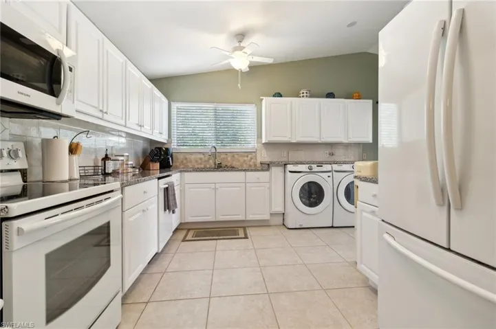 Kitchen with light tile patterned flooring, backsplash, independent washer and dryer, white appliances, and white cabinets