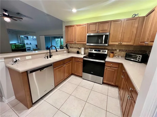 Kitchen featuring lighting on tops of cabinets, stainless steel appliances, stone tile  backsplash, sink, kitchen peninsula, and light tile patterned floors