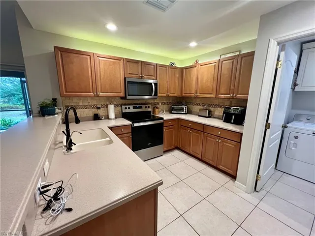 Kitchen featuring light tile patterned floors, sink, appliances with stainless steel finishes and lighting on top of cabinets.