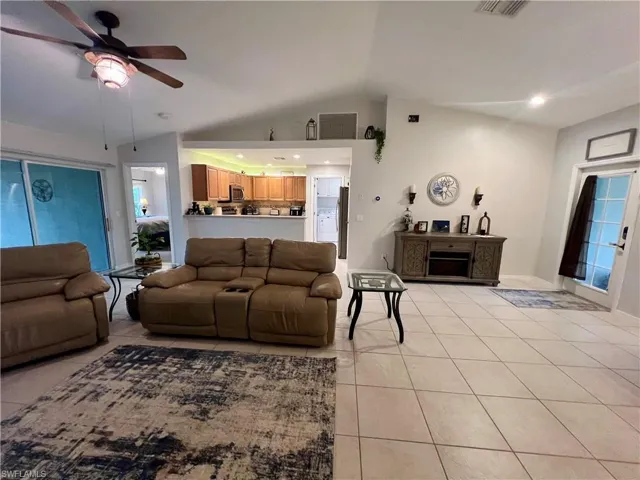 Living room with ceiling fan, light tile patterned floors, and cathedral ceilings.