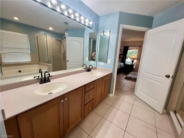 Primary bathroom with tile patterned flooring, dual sink vanity, and shower with separate jetted bathtub