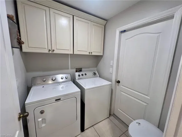 Clothes washing area with cabinets, separate washer and dryer, and light tile patterned floors