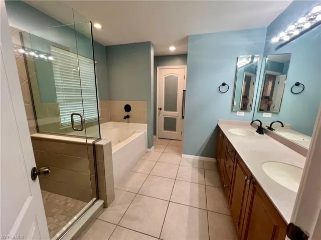 Primary bathroom with tile patterned flooring, dual sink vanity, frameless glass enclosed  shower with separate jetted bathtub