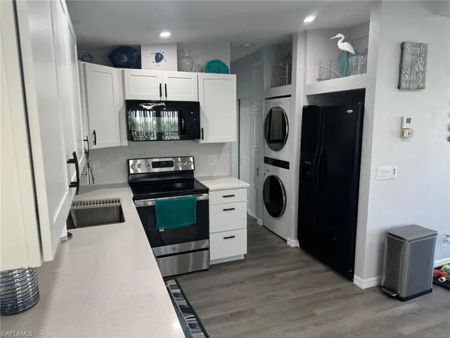 Kitchen featuring black appliances, dark hardwood / wood-style floors, white cabinetry, and stacked washer / drying machine