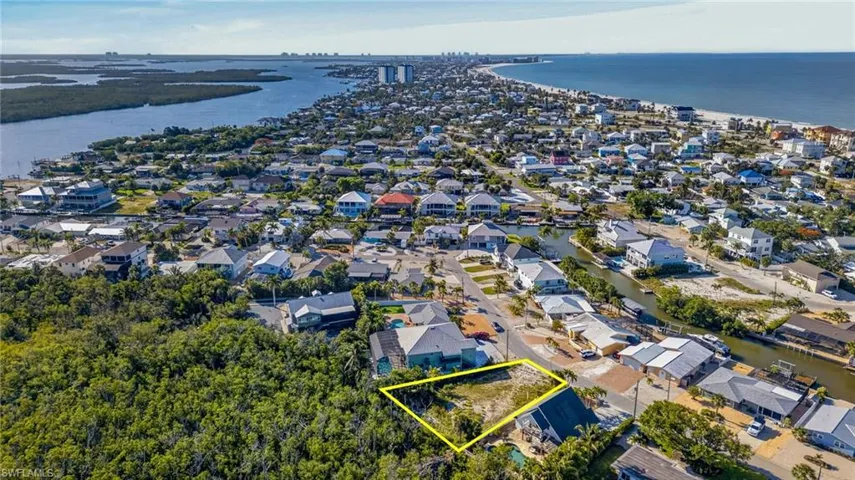 Cleared residential lot within a developed community, featuring proximity to a natural water channel, residential structures, and a sandy coastline - Virtually Edited Image