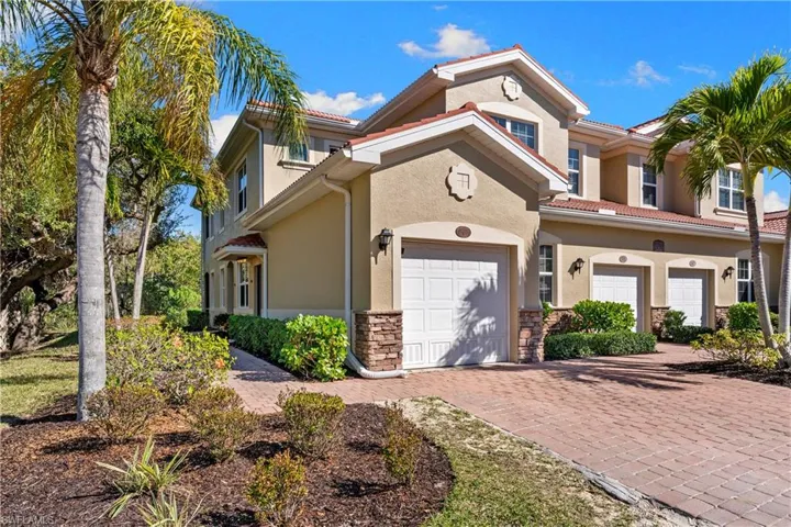 Stucco exterior featuring a tile roof, decorative stone accents, and a paved driveway