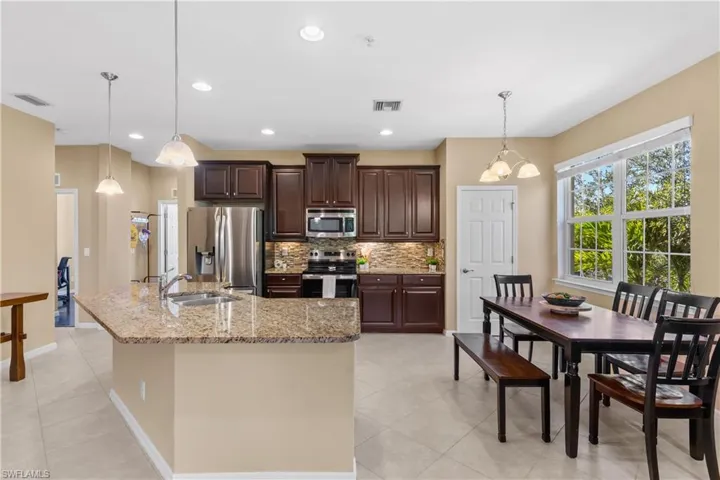 Kitchen featuring dark wood cabinetry, stainless steel appliances, a tiled backsplash, and a large central island with a granite countertop and integrated sink