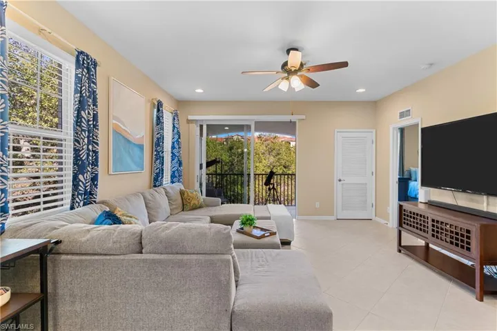 Living area featuring large windows with blinds, a sliding glass door to a balcony, recessed lighting, and a ceiling fan