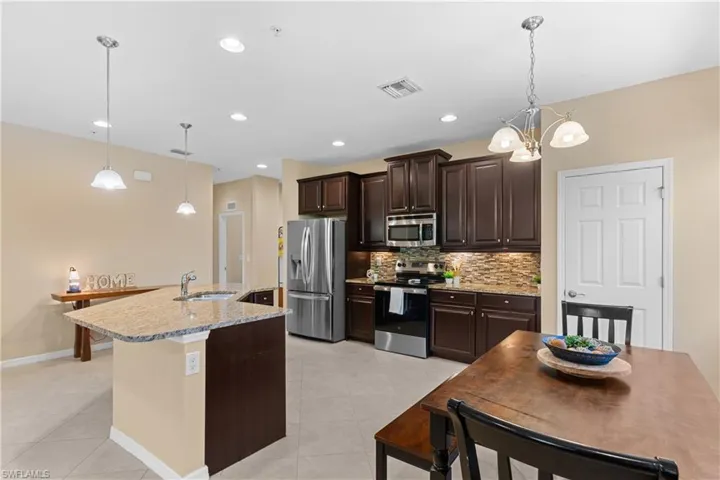 Kitchen featuring dark wood cabinetry, stainless steel appliances, granite countertops, and a tiled backsplash