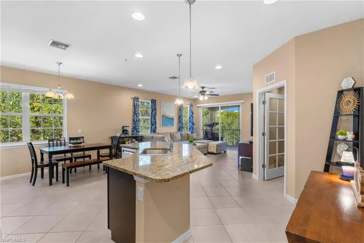 Spacious open-concept living area featuring a kitchen island with granite countertops, tile flooring, recessed lighting, and a sliding glass door leading to a balcony