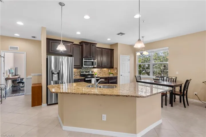 Kitchen featuring a granite-topped island with an undermount sink, dark wood cabinetry, stainless steel appliances, and a tiled backsplash