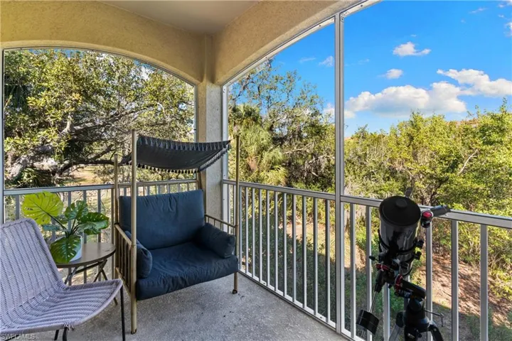 Screened balcony featuring a concrete floor, arched opening, and treetop scenery