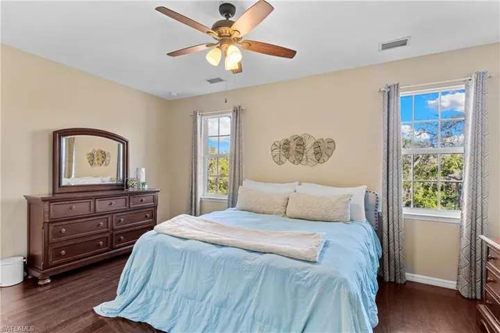 Bedroom featuring dark wood-finish flooring, light-toned walls, and a ceiling fan with integrated lighting