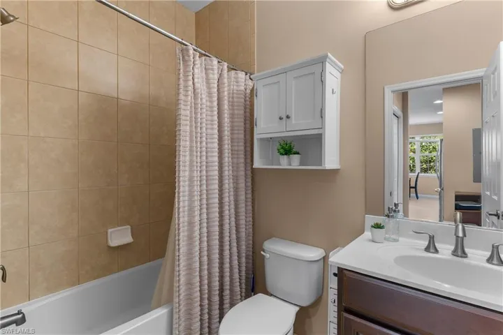 Full bathroom featuring a white porcelain tub, tan tiled shower surround, and a vanity with a white countertop and dark wood-finish cabinetry