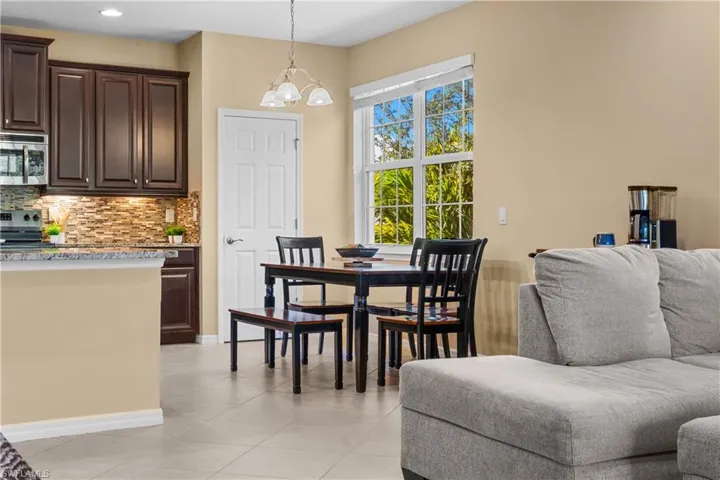 Open-concept living space with tile flooring, a kitchen peninsula, dark wood cabinetry, a tile backsplash, and a large window with exterior views