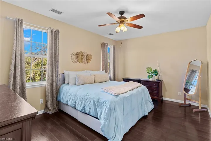 Bedroom featuring wood-finish flooring, multiple windows, a ceiling fan with integrated lighting, and neutral wall tones