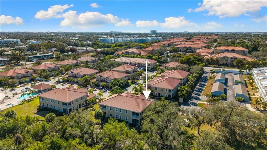 Community aerial featuring multiple residential buildings with red tile roofs, mature trees, and a distant urban skyline