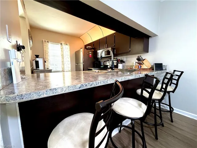 Kitchen with a breakfast bar, a peninsula, dark wood-type flooring, dark wood finish cabinets, and stainless steel appliances
