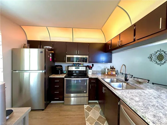 Kitchen with stainless steel appliances, light countertops, light wood-type flooring, and dark wood finish cabinets