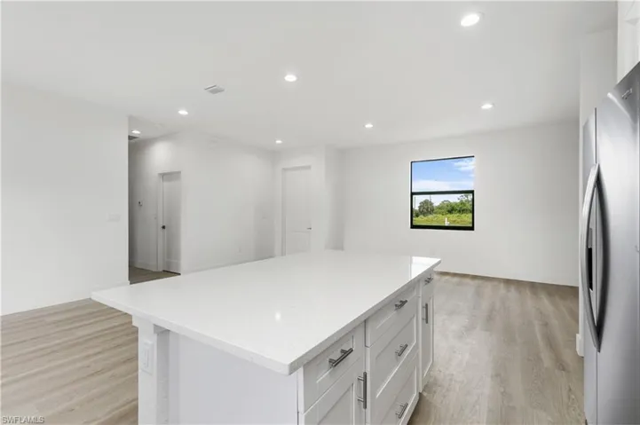 Kitchen featuring white cabinetry, light hardwood / wood-style floors, a center island, and stainless steel fridge