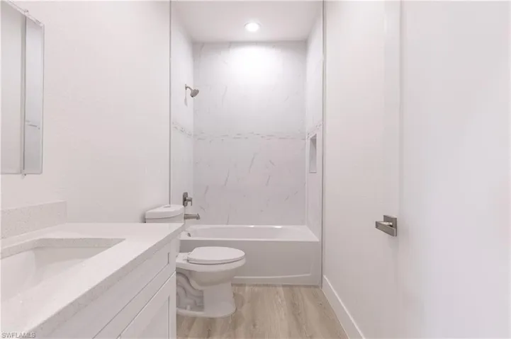 Full bathroom with vanity, hardwood / wood-style flooring, toilet, and tiled shower / bath combo