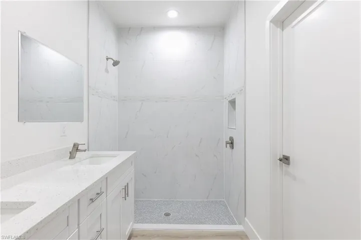 Bathroom featuring dual vanity, tiled shower, and wood-type flooring