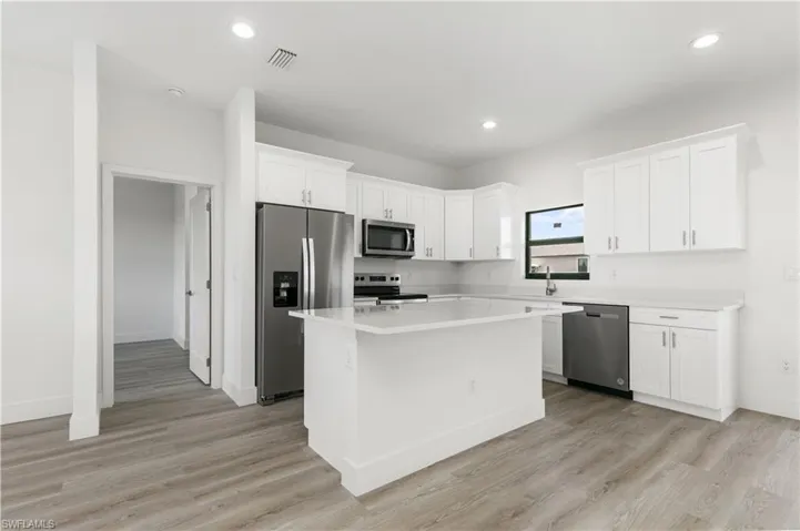 Kitchen with light hardwood / wood-style flooring, white cabinets, a kitchen island, and appliances with stainless steel finishes