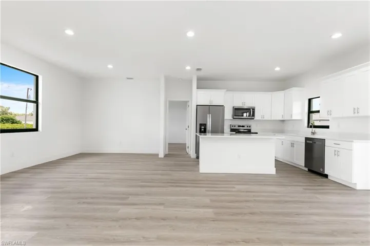 Kitchen with light hardwood / wood-style floors, white cabinets, a kitchen island, and stainless steel appliances