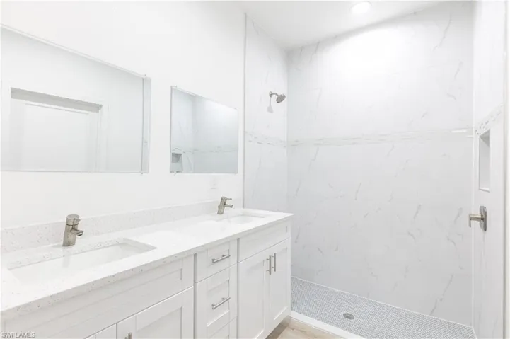 Bathroom featuring tiled shower and double vanity