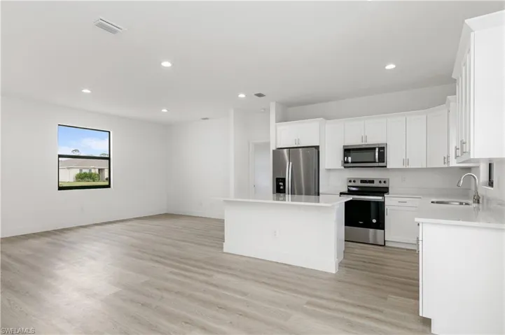 Kitchen featuring light hardwood / wood-style floors, stainless steel appliances, a center island, sink, and white cabinetry