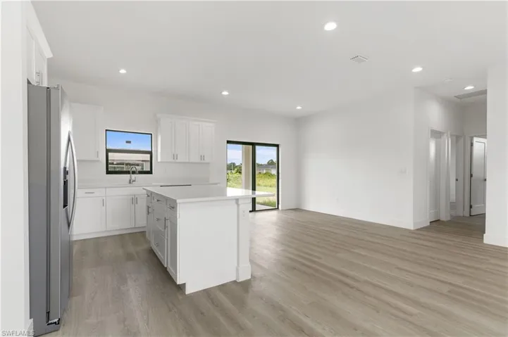 Kitchen with stainless steel fridge with ice dispenser, a kitchen island, white cabinetry, light wood-type flooring, and sink