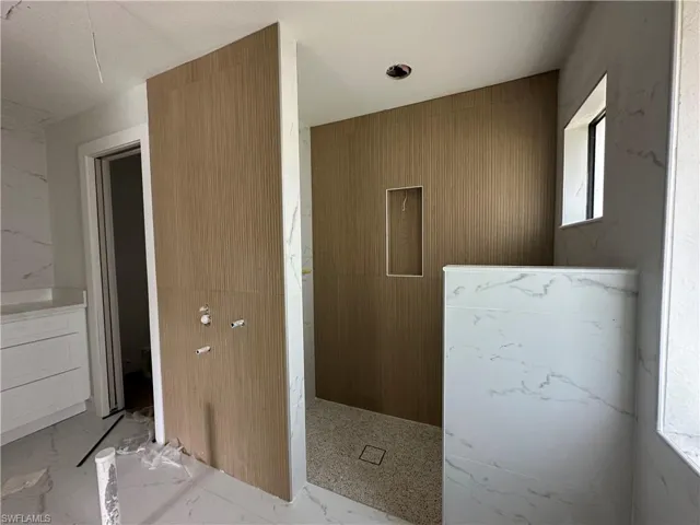 Shower space featuring large-format veined wall panels, wood-finish ribbed tile accents, a recessed wall niche, and mosaic tile flooring
