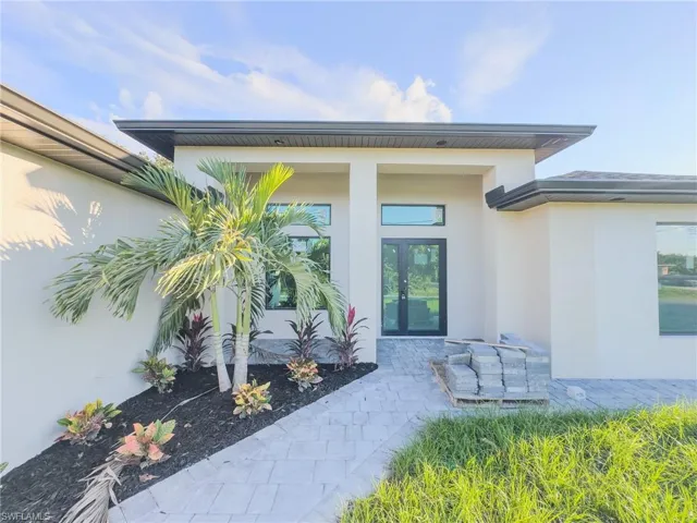Modern stucco exterior featuring a covered entryway, dual-pane glass front door with transom window, and paver walkway