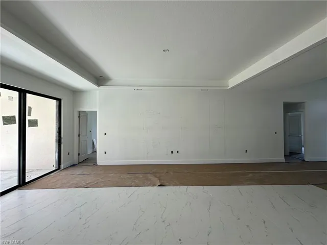 Open-concept interior featuring a recessed tray ceiling, large-format tile flooring with marble-style veining, and floor-to-ceiling sliding glass doors