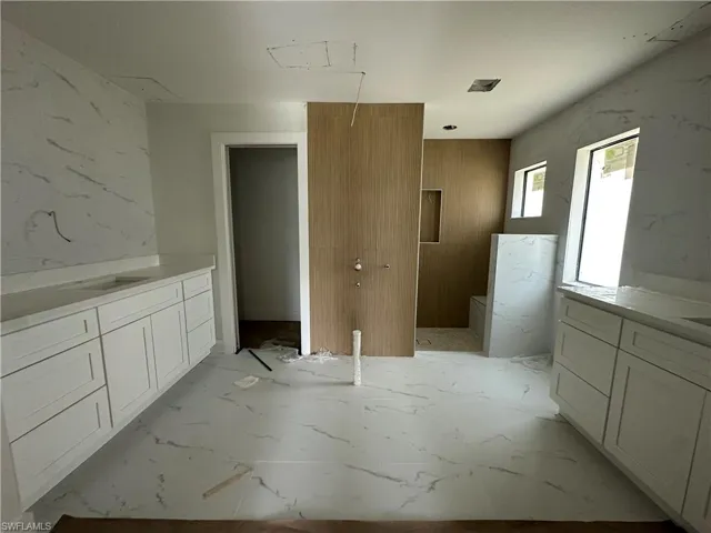 Dual white vanities with integrated sinks and white stone-patterned countertops, wood-finish wall paneling, walk-in shower with stone-patterned tile surround, and coordinating stone-patterned flooring