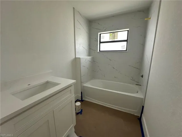 Bathroom featuring a white vanity cabinet with an integrated rectangular sink, solid-surface countertop, and a built-in tub with stone-finish tile surround