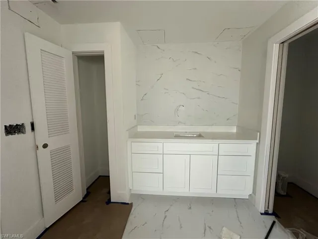 Vanity featuring white shaker-style cabinetry, solid-surface countertop with an integrated sink, and full-height stone-look wall cladding