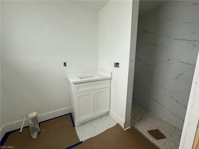 Bathroom featuring a white vanity cabinet with a stone-top integrated sink, walk-in shower with large-format wall tile, and stone-finish floor tile