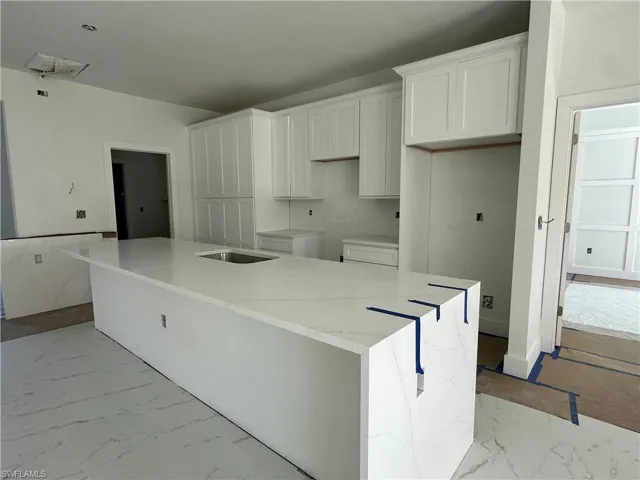 Kitchen featuring a waterfall-edge island with stone-finish countertops, white shaker-style cabinetry, and large-format tile flooring
