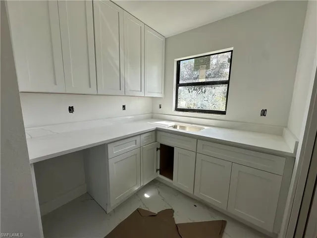 Shaker-style white cabinetry, solid-surface countertops with matching backsplash, undermount stainless steel sink, and large-format rectified tile flooring