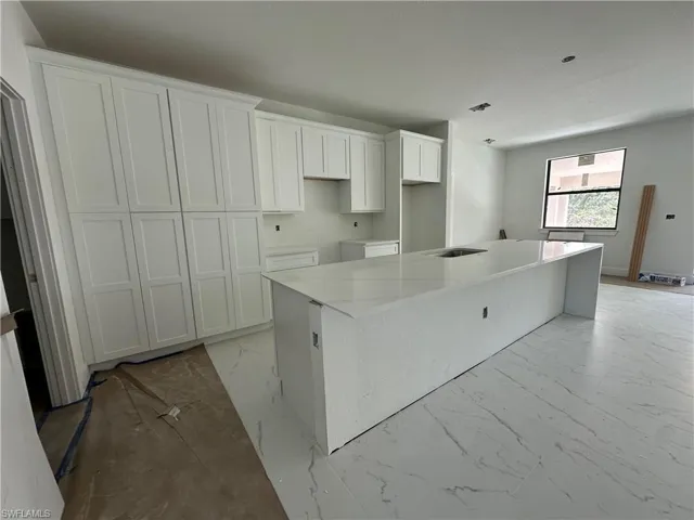 Kitchen featuring floor-to-ceiling Shaker-style cabinetry, a waterfall island with stone-finish countertop, and large-format tile flooring