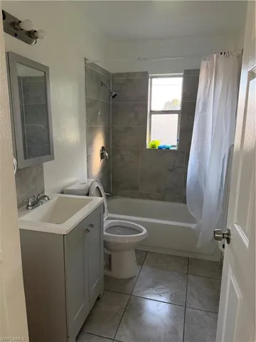 Bathroom featuring vanity, shower / bath combo with shower curtain, light tile patterned flooring, and a textured wall